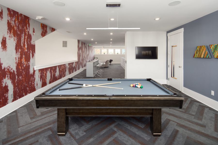 Modern game room with a pool table, pool cues, and billiard balls, featuring stylish decor and seating area.