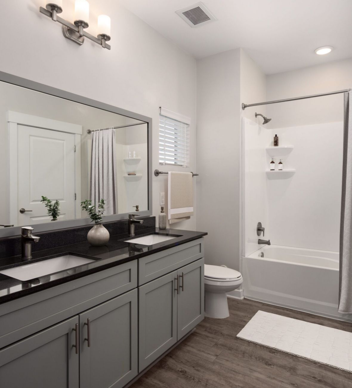 Modern bathroom with dual sink vanity, large mirror, bathtub with shower curtain, and wooden floor.