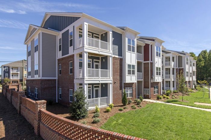 Modern three-story apartment buildings with balconies and landscaped lawns on a sunny day.