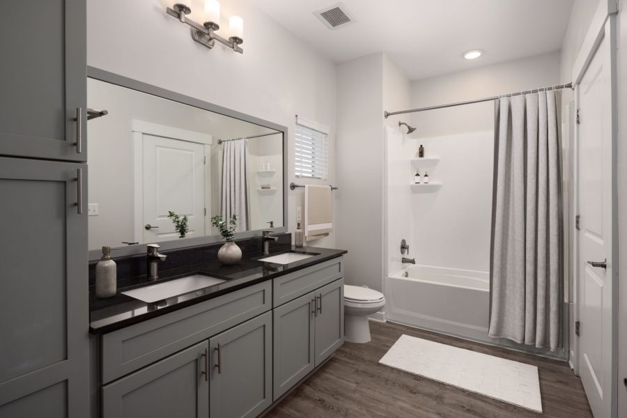 Modern bathroom with dual sink vanity, large mirror, bathtub with shower curtain, and wooden floor.