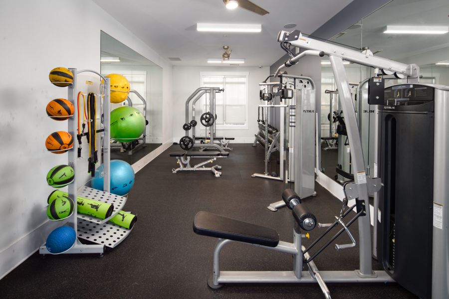 Modern gym with weight machines, medicine balls, dumbbells, and mirrors along the wall.