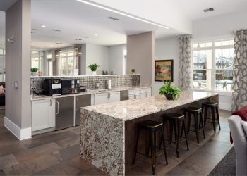 Modern kitchen with granite island, bar stools, stainless appliances, and large windows with patterned curtains.