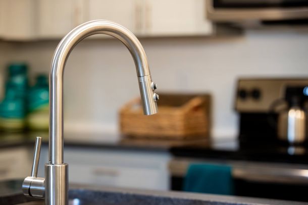Proximity Northlake Close-up of a modern stainless steel kitchen faucet with a blurred stove and counter in the background.