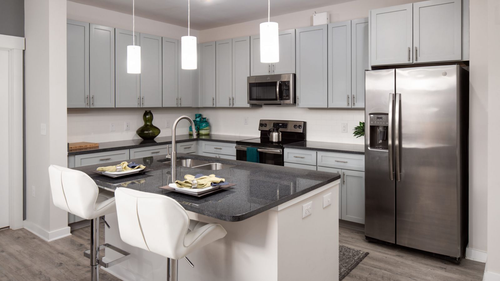 Modern kitchen and living area with white cabinets, stainless steel appliances, and a large island. Cozy seating area with a sofa and rug in the background. Bright and inviting atmosphere.