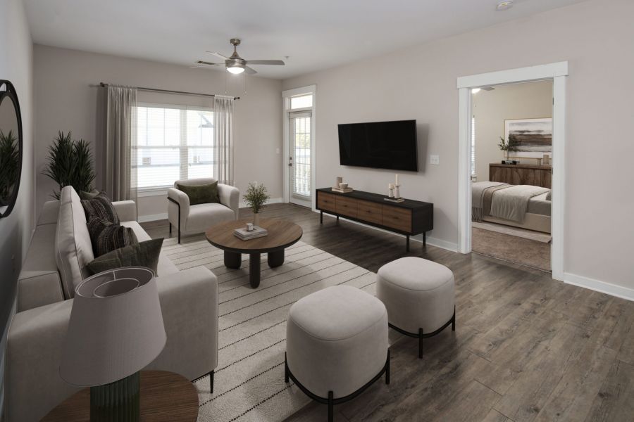 Modern living room with neutral décor, a TV on the wall, and a view into a furnished bedroom.