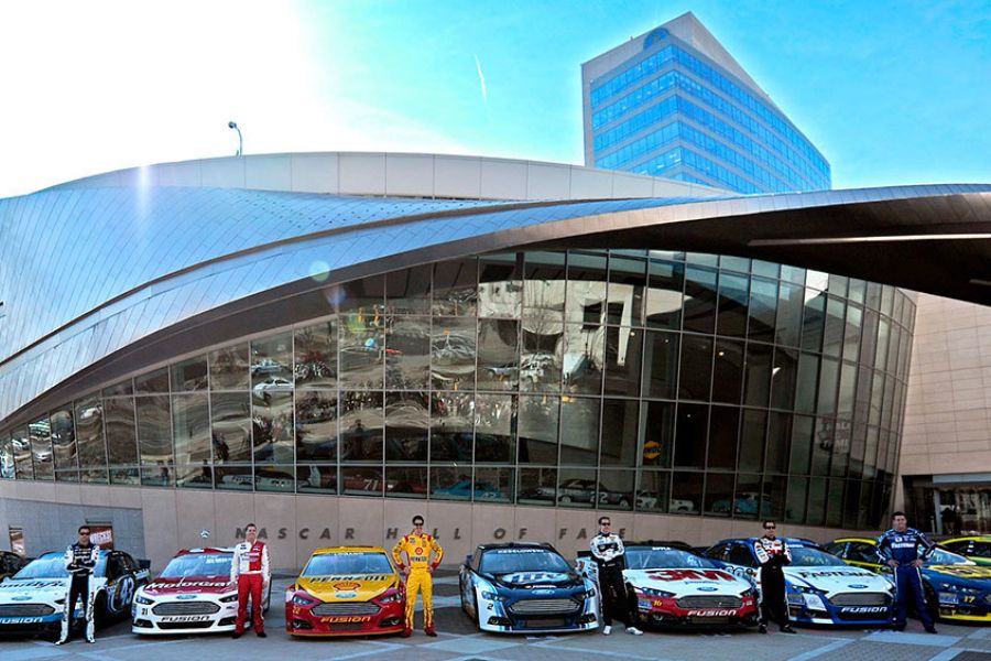 Proximity Northlake Nine NASCAR stock cars and their drivers are lined up in front of the NASCAR Hall of Fame building.