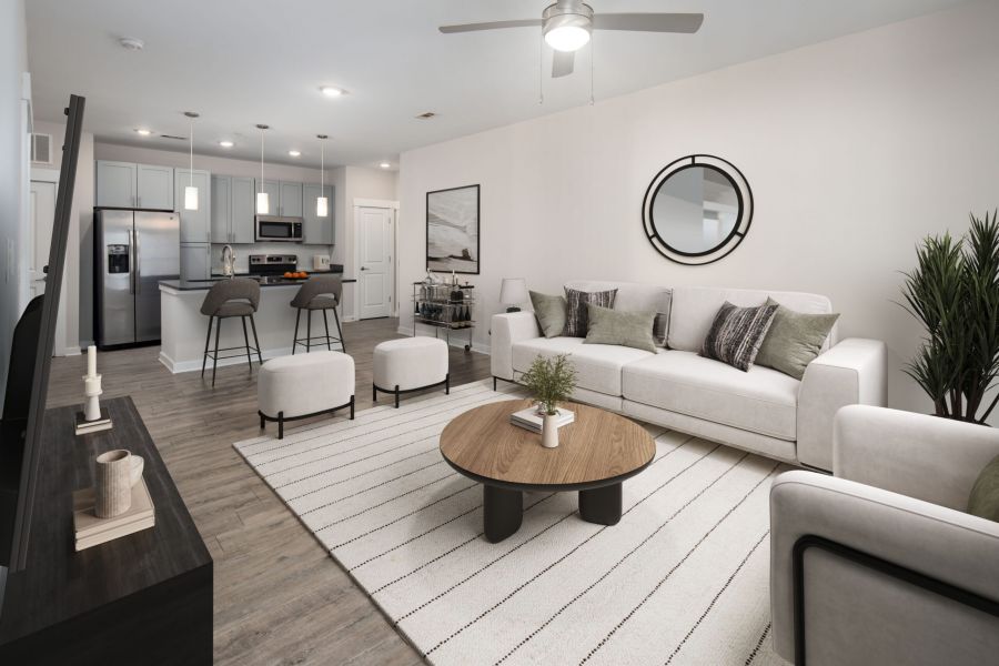 Modern living room with a sofa, coffee table, TV, and open kitchen with bar stools in the background.