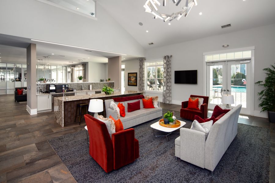 Modern open-concept living area with gray sofas, red chairs, kitchen, and large windows overlooking a pool.