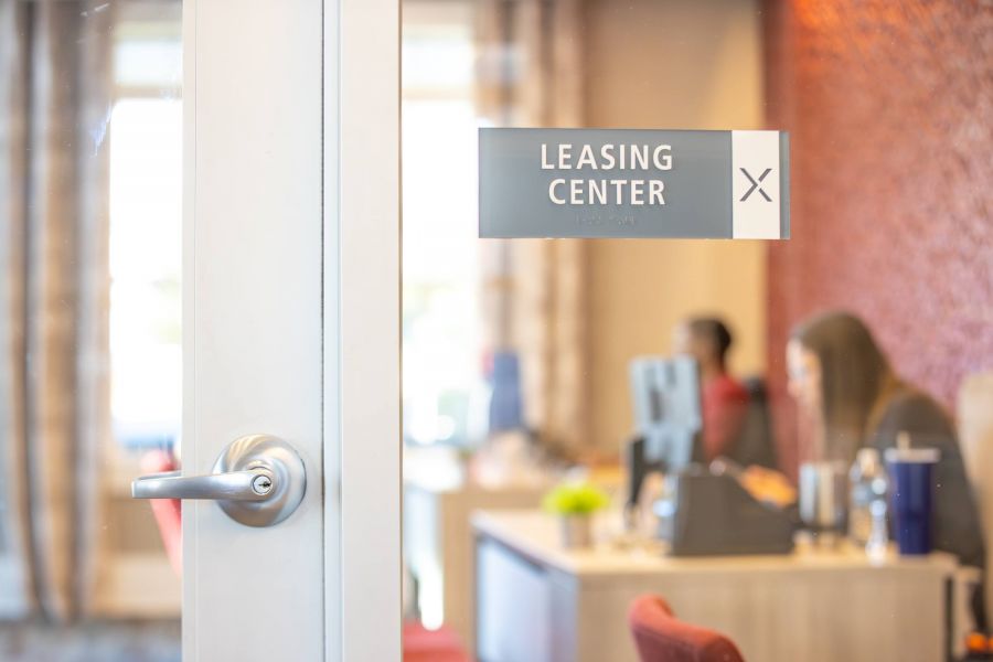 Proximity Northlake Glass door with a "Leasing Center" sign; two people working at desks are visible inside.