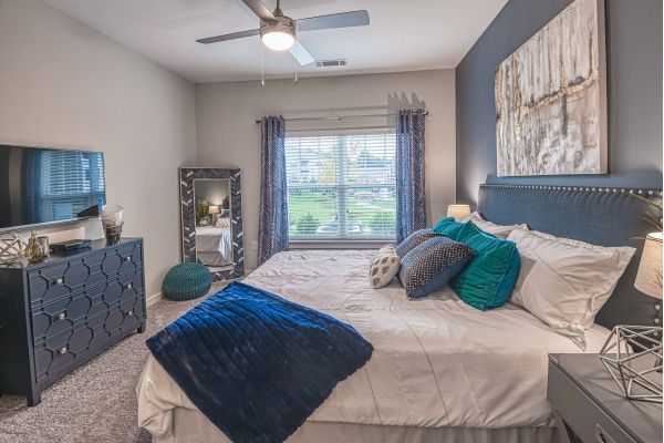 Proximity Northlake Modern bedroom with a large bed, blue accents, dresser, mirror, and a window letting in natural light.