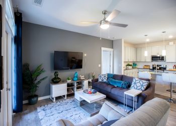 Proximity Northlake Modern living room with a gray accent wall, TV, sofas, and open kitchen with bar stools in the background.
