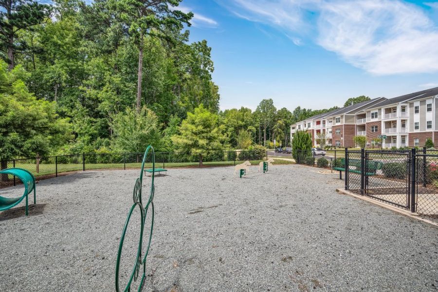 Proximity Northlke Fenced dog park with agility equipment, gravel ground, trees in the background, and apartments nearby.