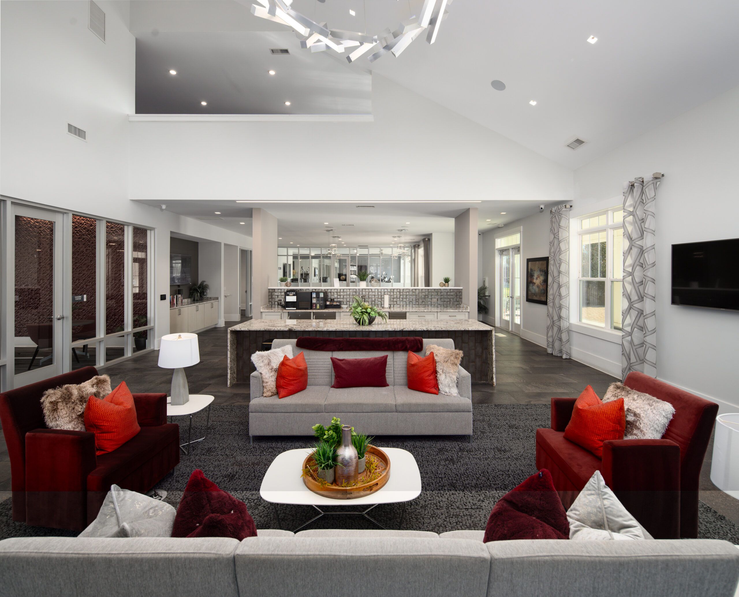 Modern living room with gray and red sofas, white tables, and open kitchen in the background.