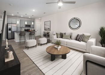 Modern living room with a sofa, coffee table, TV, and open kitchen with bar stools in the background.