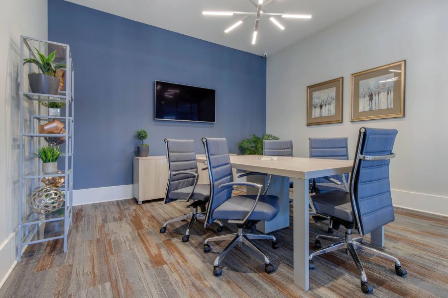 Modern conference room with blue chairs, a large table, wall art, TV, and decorative plants on shelves.